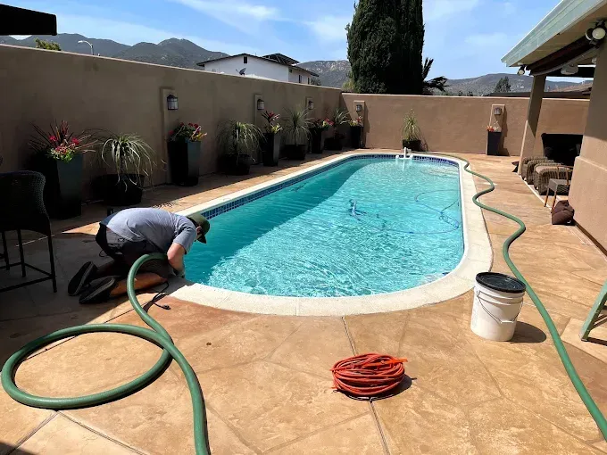 Person cleaning a backyard swimming pool with a hose on a sunny day