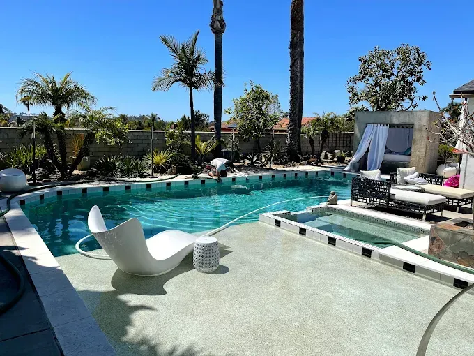 Backyard pool with white lounge chairs, palm trees, and a sunny patio area