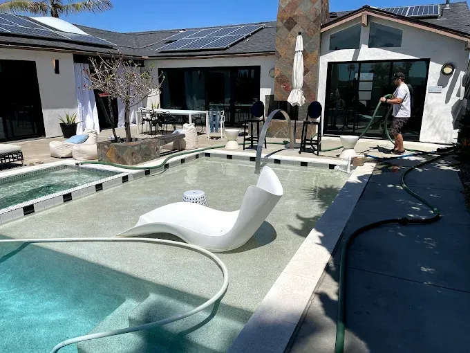 Pool cleaning scene with floating vacuum hose, solar-covered roof, and a person near the patio.
