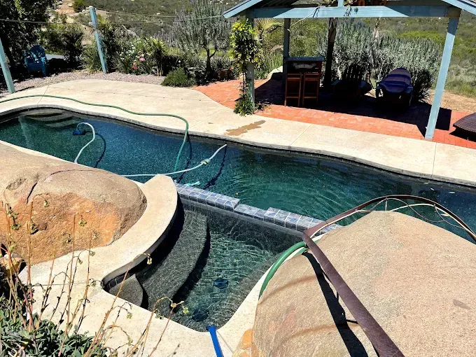 Backyard swimming pool with curved rock edges and a shaded patio area