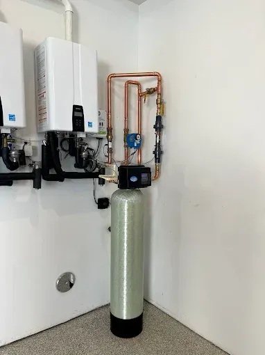 Water heater and plumbing pipes in a utility closet with a tall green tank in front