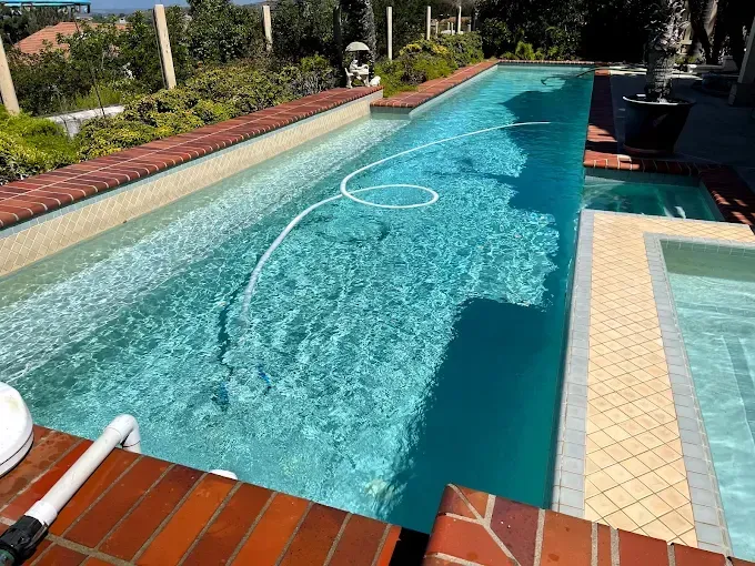 Long turquoise swimming pool beside a tiled deck and lush garden in bright sunlight