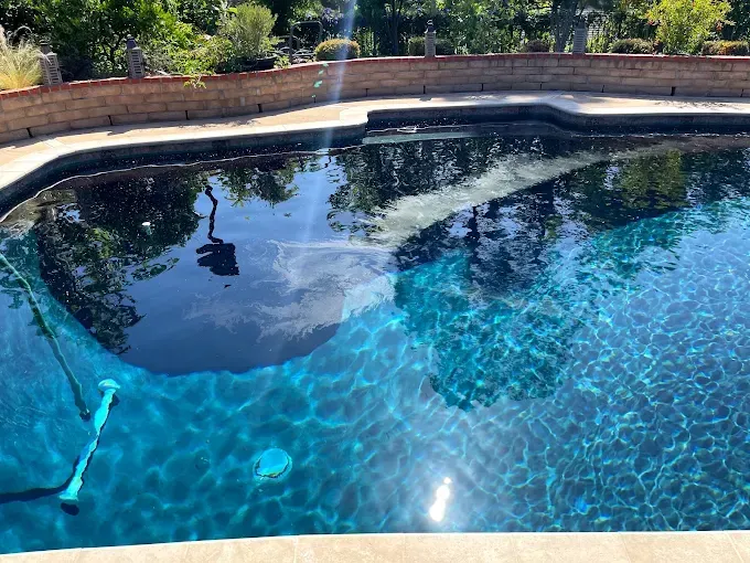 Sunny backyard swimming pool with clear blue water and deck landscaping reflections