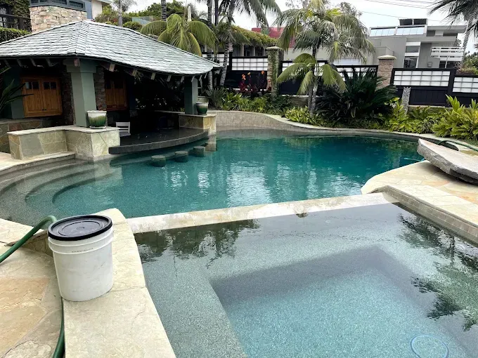 Resort-style pool with a spa, stone decking, and a shaded pool bar surrounded by tropical plants
