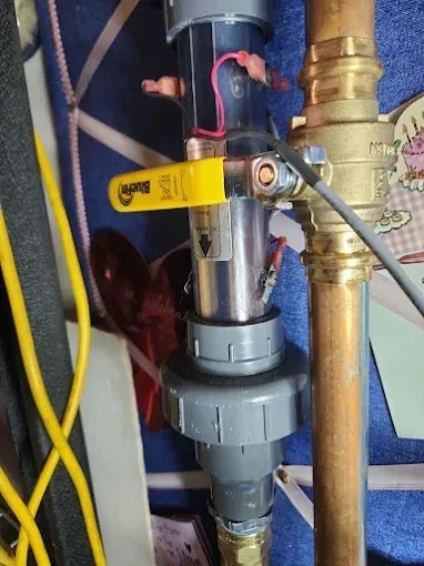 Close-up of yellow-handled valve and plumbing pipes against a blue wall