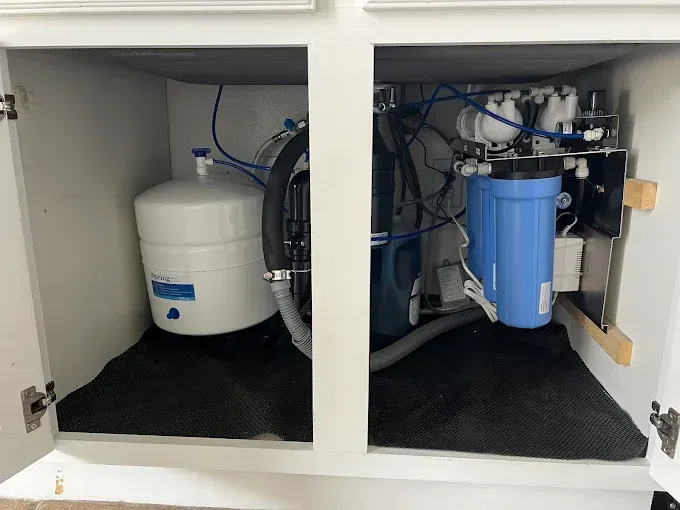 Under-sink water filtration system with white and blue tanks and exposed pipes in a cabinet