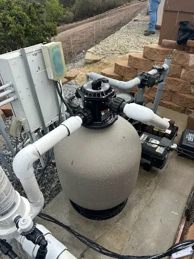 Pool filter and plumbing on a concrete pad beside a brick wall outdoors