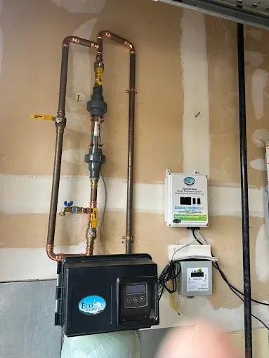 Utility meter and black wall-mounted unit with copper pipes and valves in a basement.