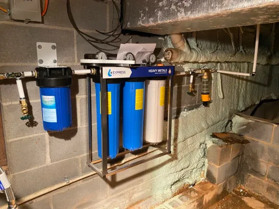 Blue water filter system mounted on a basement wall next to exposed pipes and concrete blocks