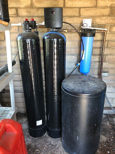 Water softener and filtration system with black tanks and a blue filter in a utility room