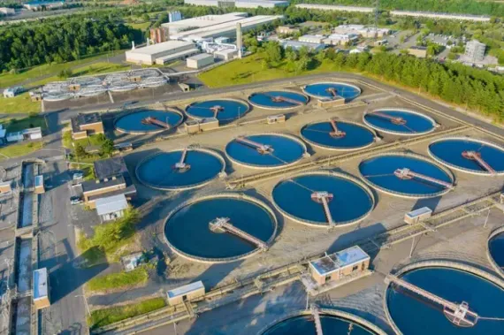 Aerial view of a wastewater treatment plant with circular blue settling tanks and surrounding greenery