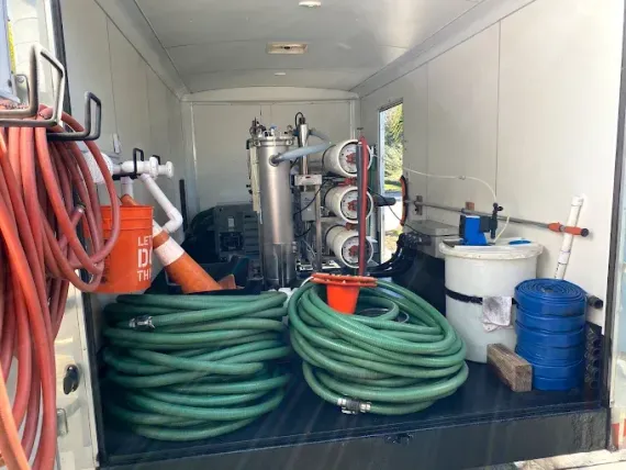 Industrial room with coiled green and red hoses, tanks, and cleaning equipment arranged along the walls