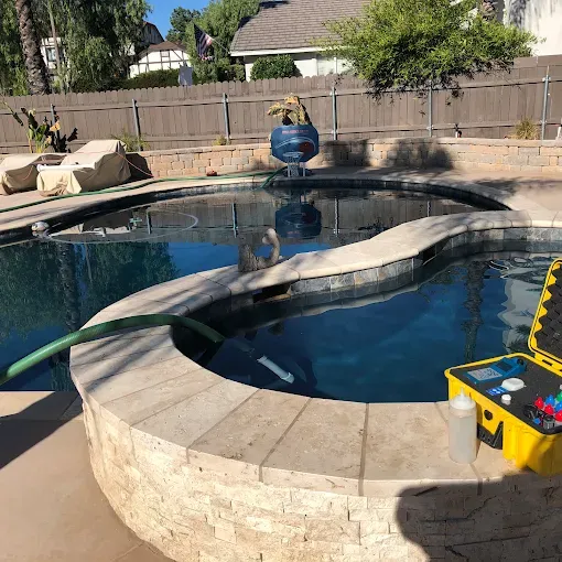 Backyard swimming pool with a hot tub, stone coping, and pool cleaning equipment on the edge