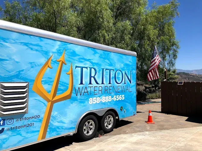 Triton Water Renewer truck parked outdoors beside an American flag and orange traffic cone