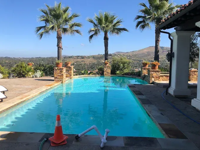 Backyard pool with palm trees, mountains, and a patio chair in bright sunlight