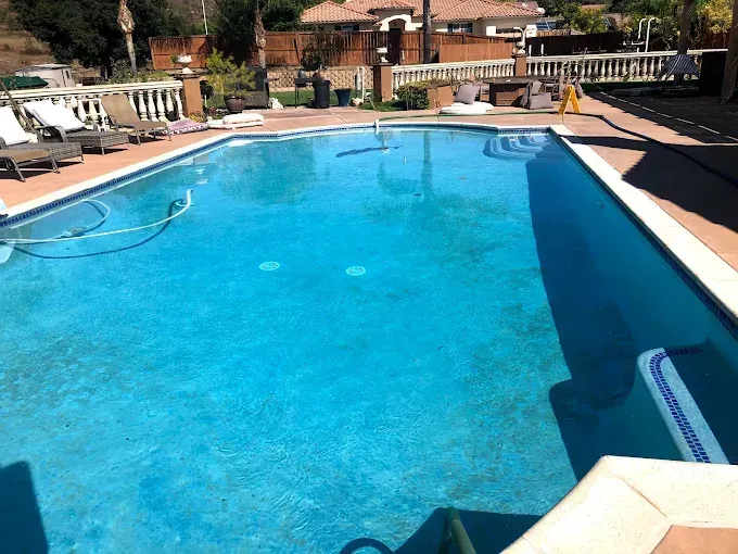 Outdoor swimming pool with bright blue water, lounge chairs, and buildings in the background