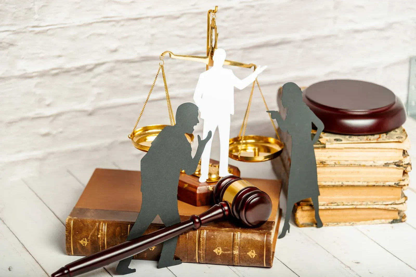 Silhouette figures arguing near a judge's gavel, scale, and books.  White figure in balance scale.