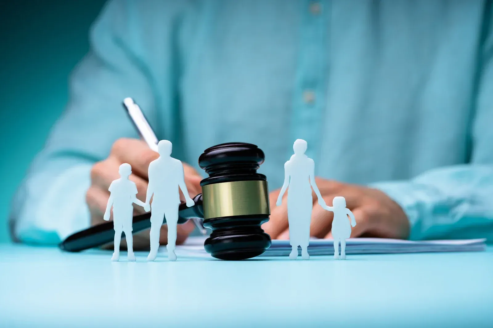 Person with a pen, gavel, and family cutouts on a desk, possibly related to legal proceedings.