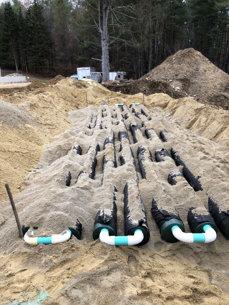 Construction site: trenches filled with black pipes, sand, and white PVC pipes.