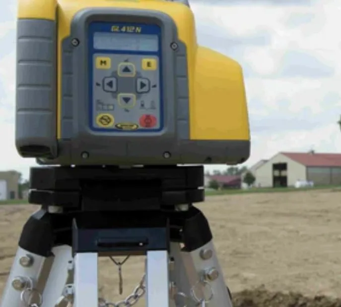 Yellow and gray laser level on a tripod, outdoors on a construction site.