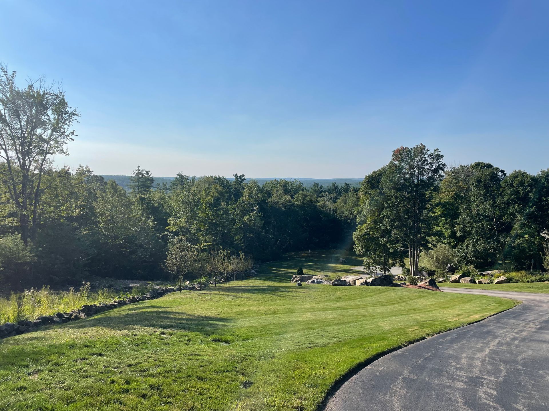 Green grassy lawn slopes towards a tree-filled horizon under a clear blue sky.