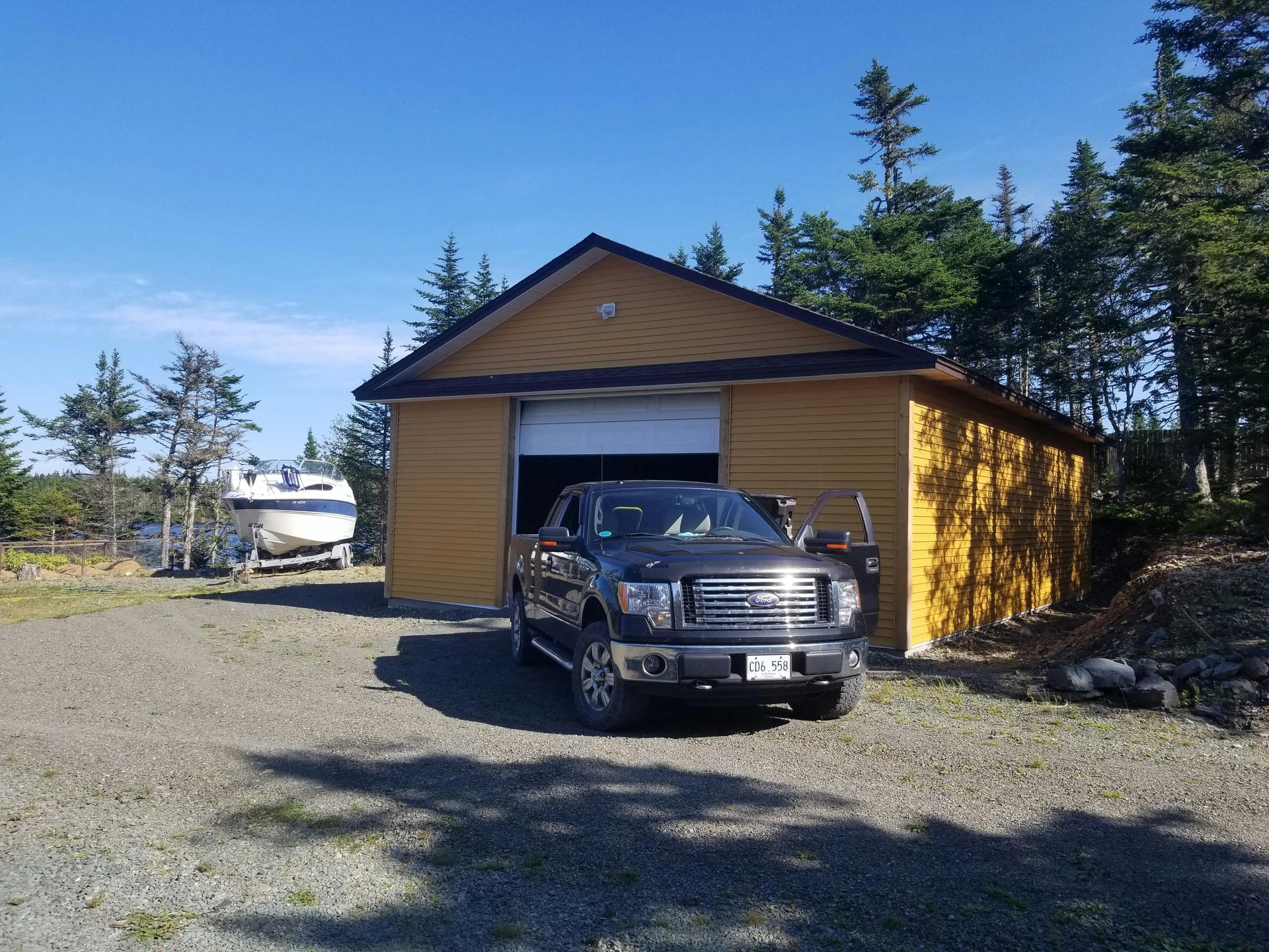 A dark pickup truck parked in front of an open garage, a boat on a trailer to the left.
