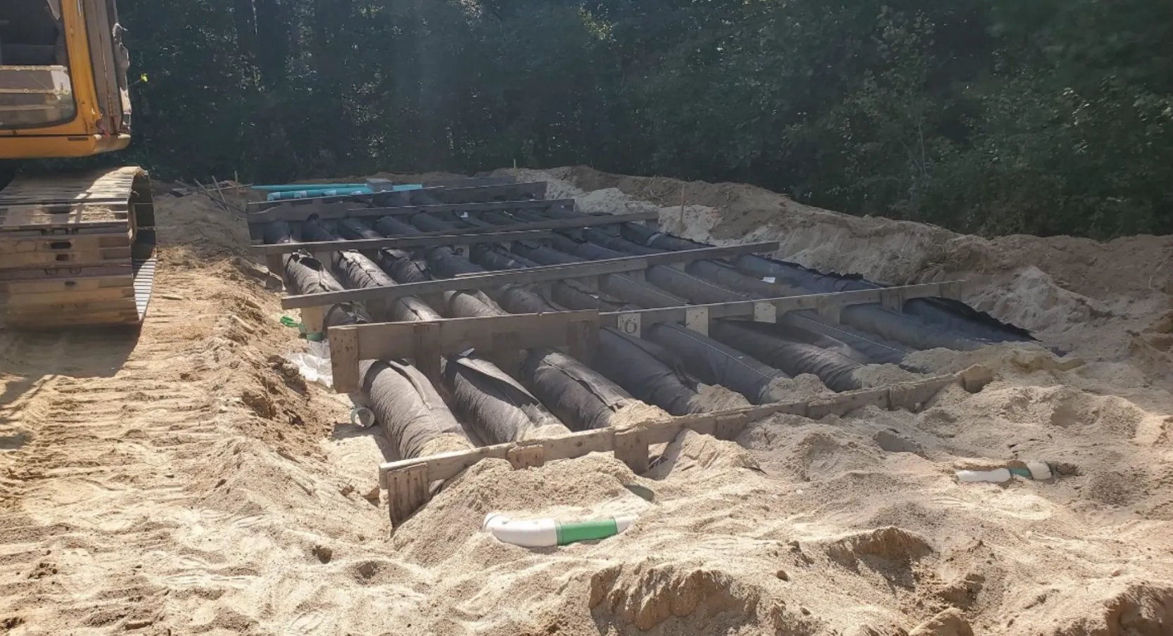 Excavated area with parallel pipes installed in the ground; heavy machinery visible; daylight setting.