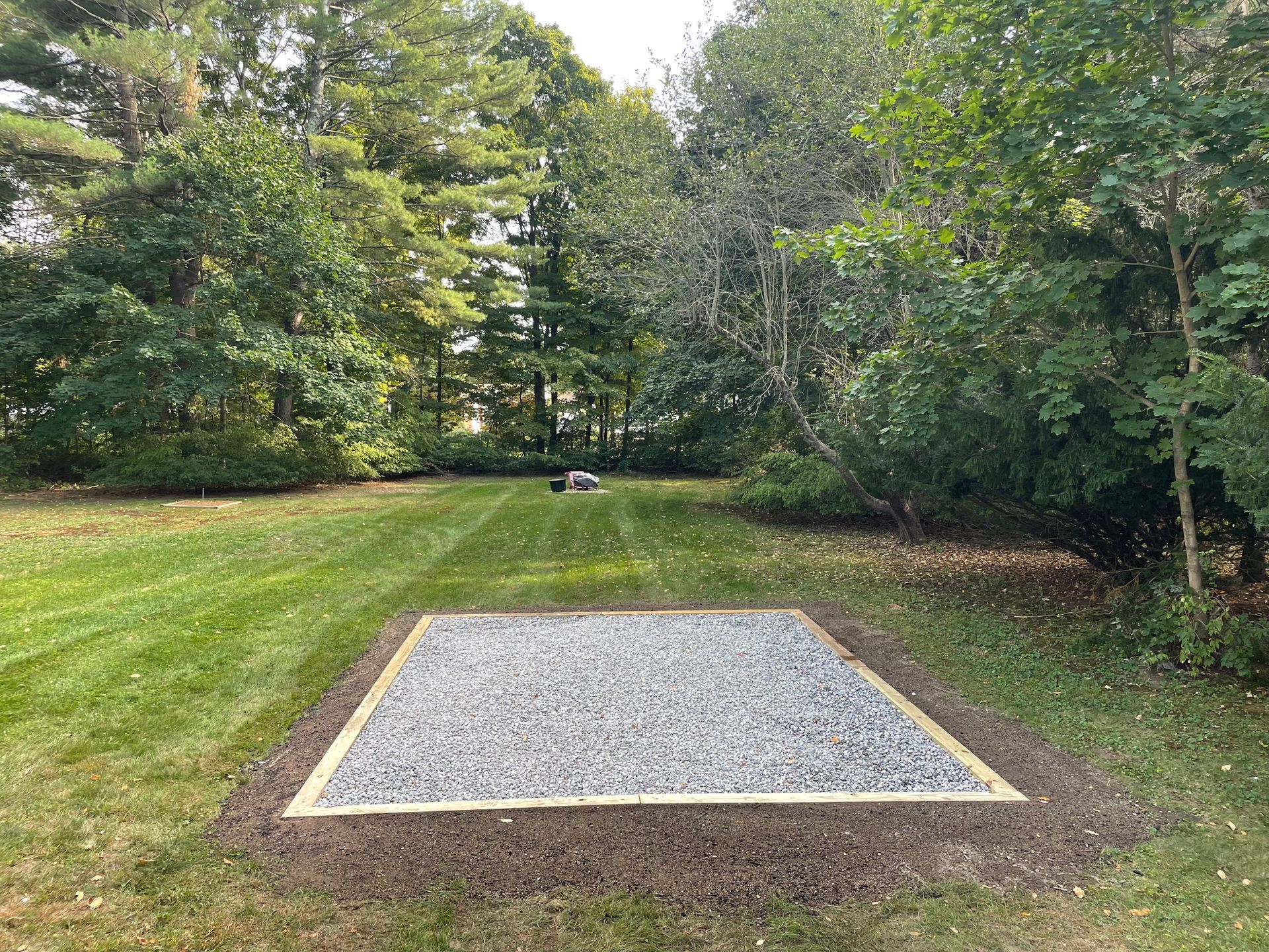 Gravel-filled square bordered with wood in a grassy yard, with trees in the background. 