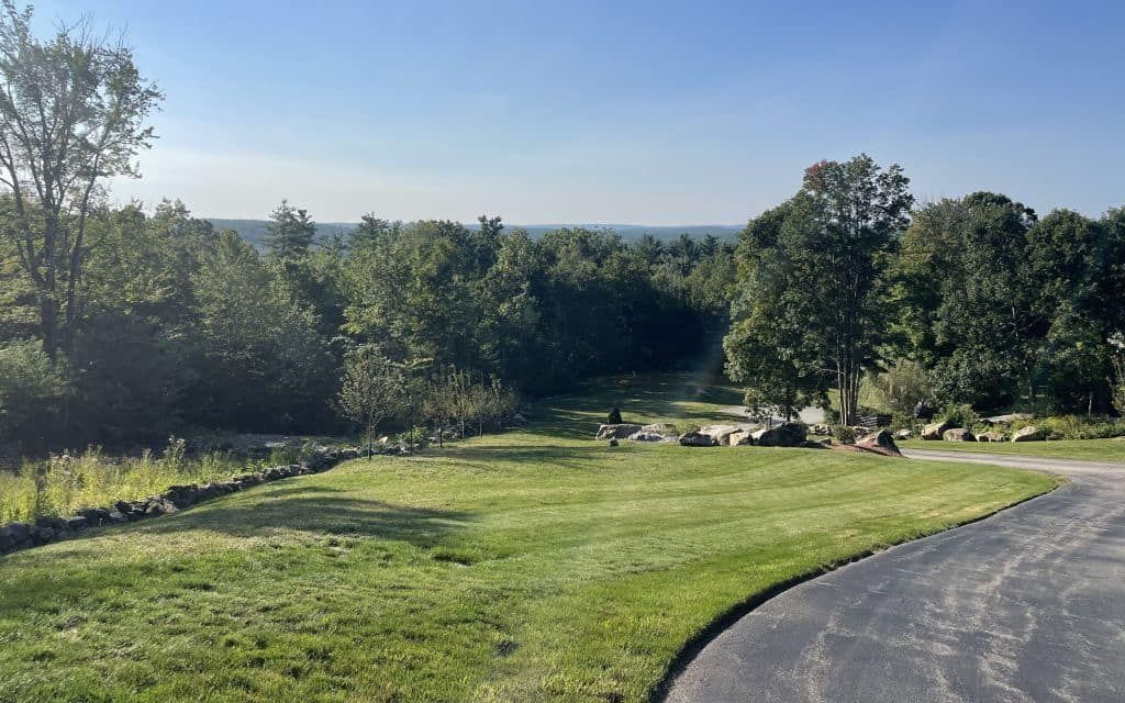 Concrete foundation under construction next to an existing house, surrounded by dirt and trees.