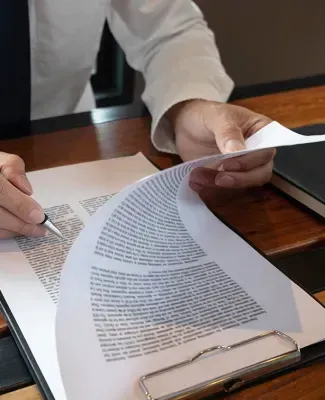 Person holding and examining documents on a desk, pen in hand, focused.