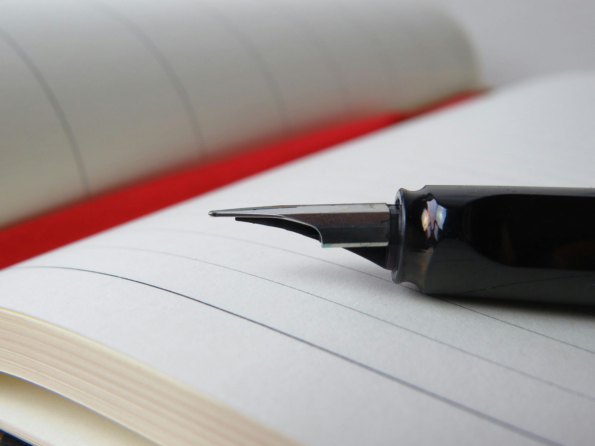 Fountain pen on an open notebook with lined pages. Close-up view, black pen, white pages.