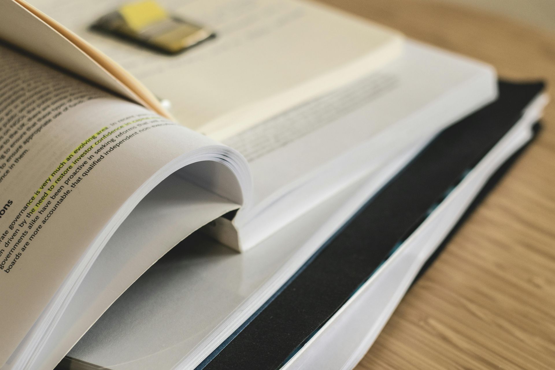 Stack of open books with highlighted text and a sticky note, on a wooden surface.