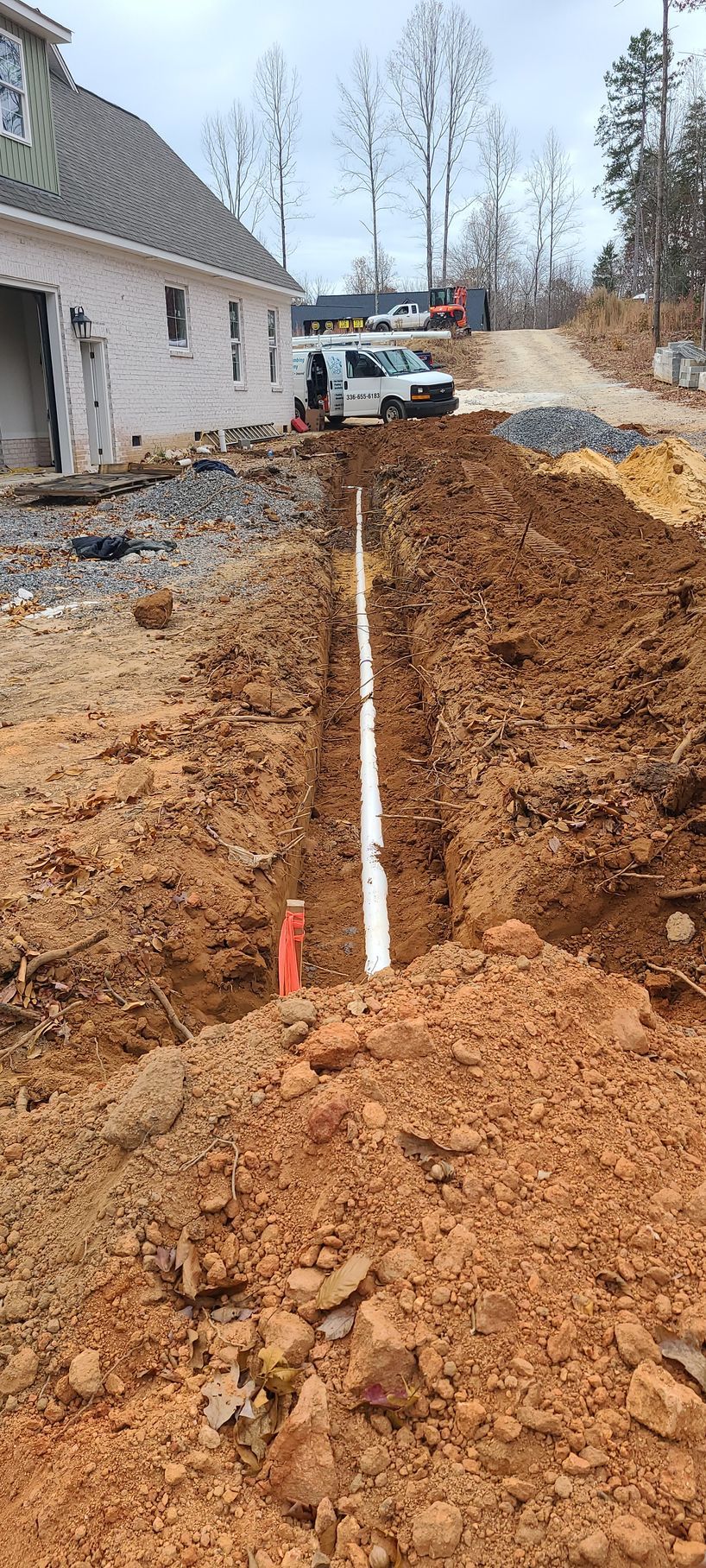A white truck is driving down a dirt road next to a house under construction.