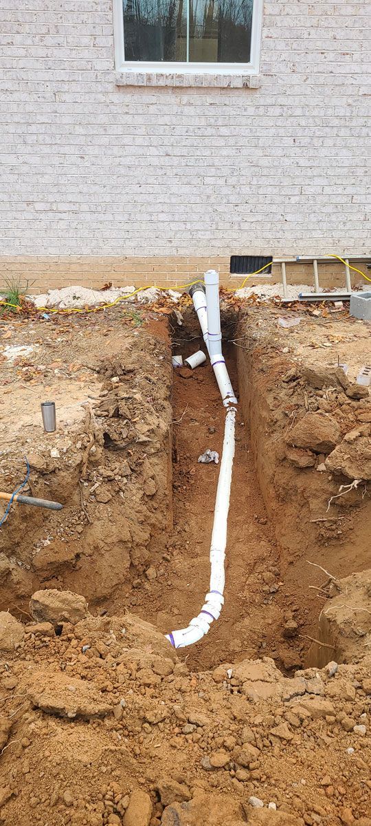 A drain pipe is being installed in the dirt in front of a house.
