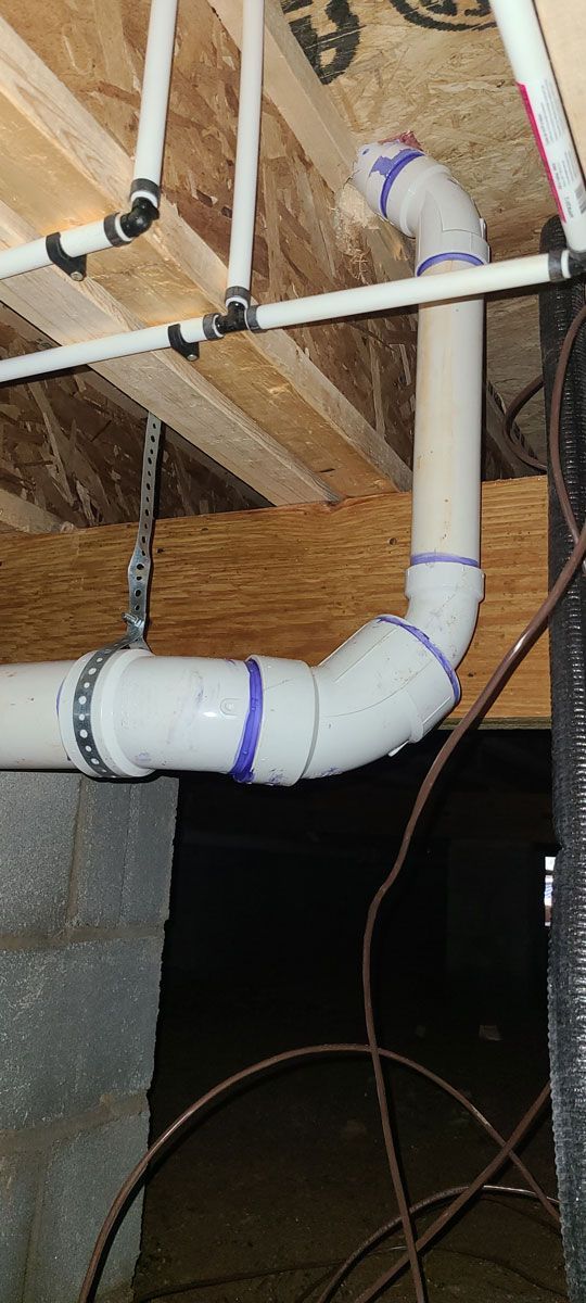 A close up of a pvc pipe in a basement under a wooden ceiling.