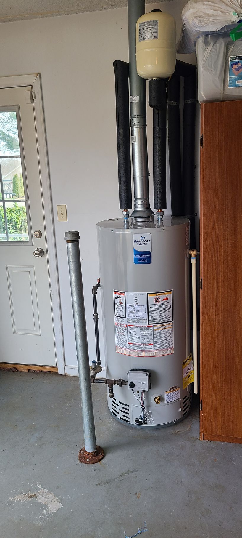 A gas water heater is sitting in a garage next to a door.