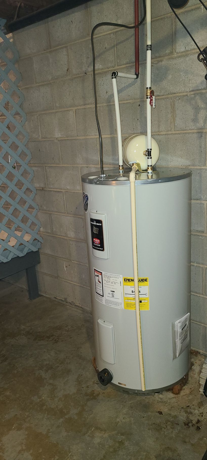 A water heater is sitting in a basement next to a brick wall.
