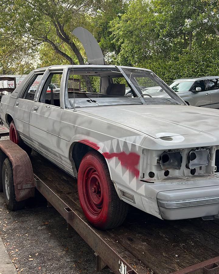 A white car with red wheels is on a trailer.
