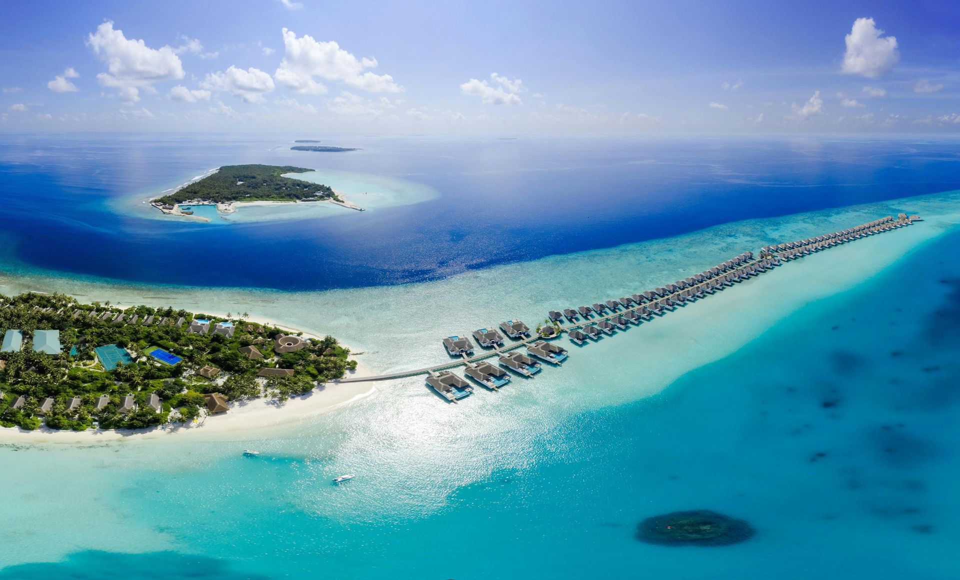 Aerial view of Maldivian resort with overwater bungalows, turquoise water, and islands in the distance.