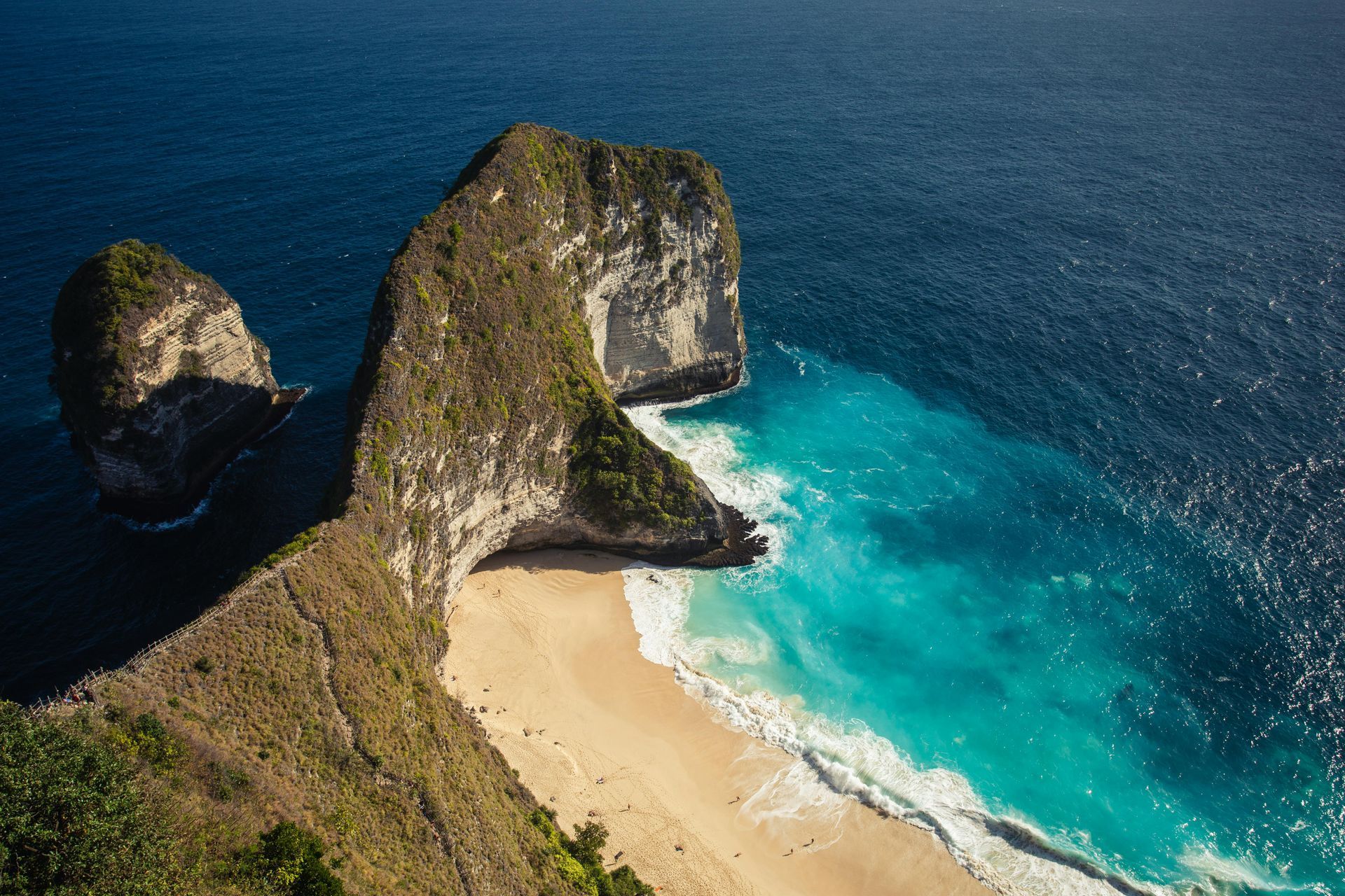 Cliffside beach with white sand and turquoise water meeting dark blue ocean.
