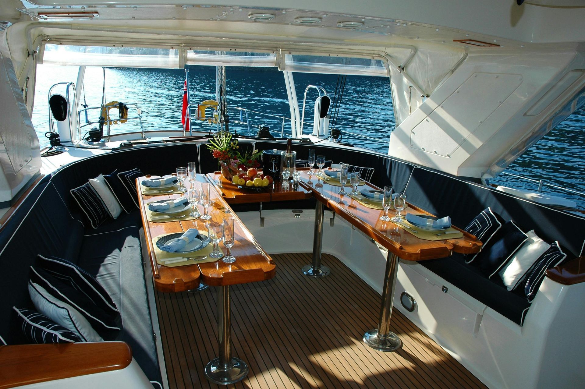 Dining area on a yacht, with wooden tables set for a meal. Windows show the sea.