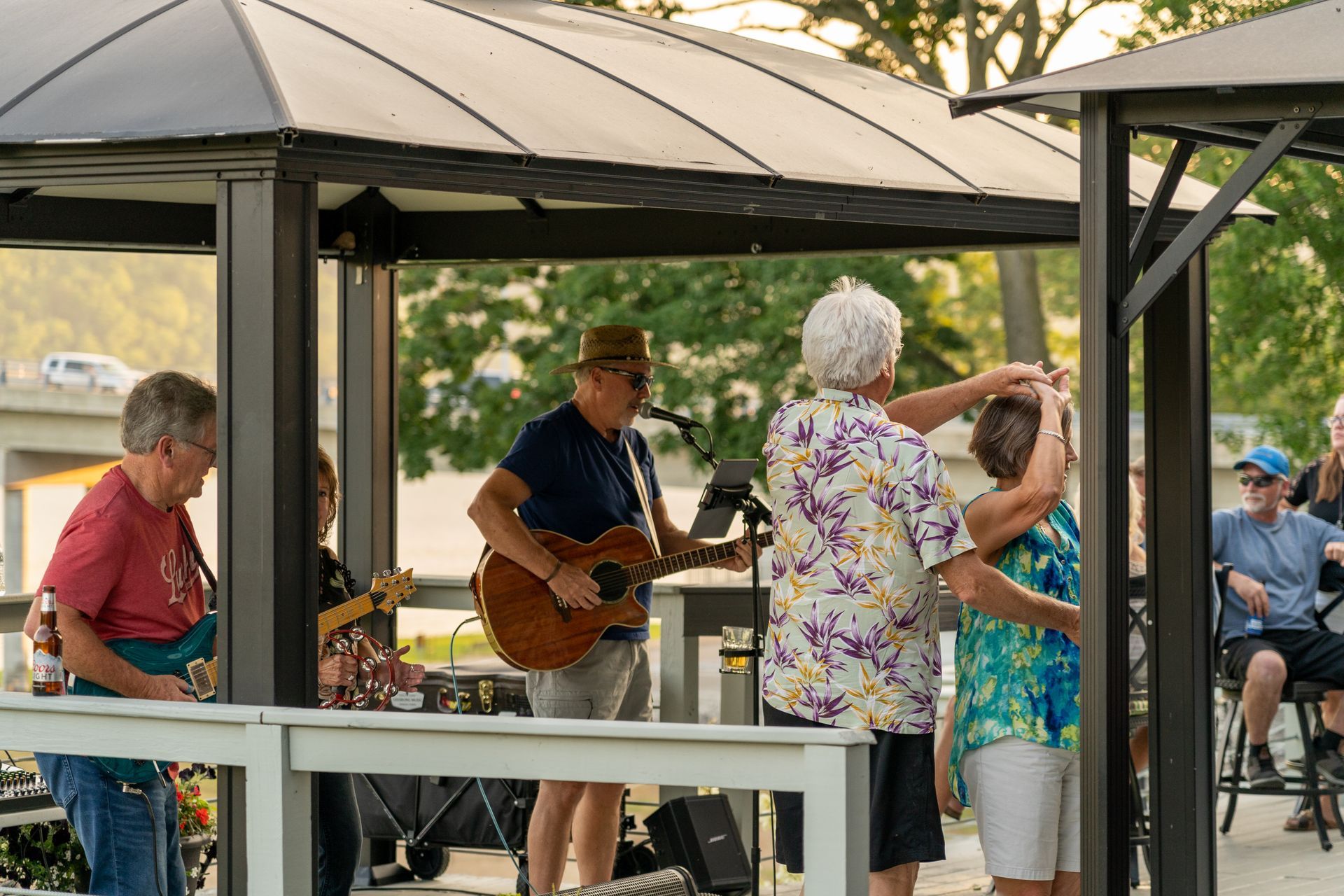 A group of people are dancing under a gazebo while a man plays a guitar.