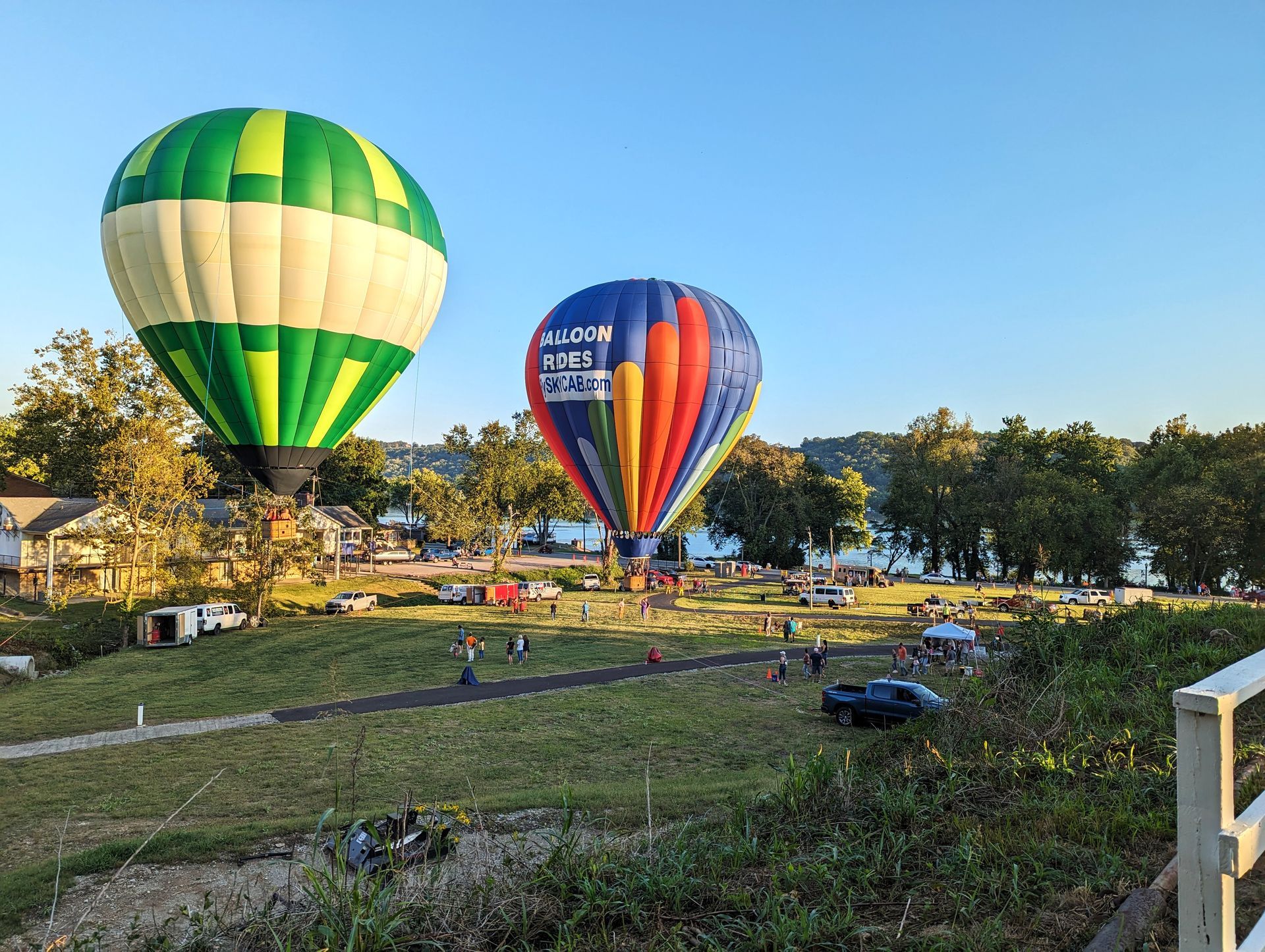 Two hot air balloons are flying over a grassy field.