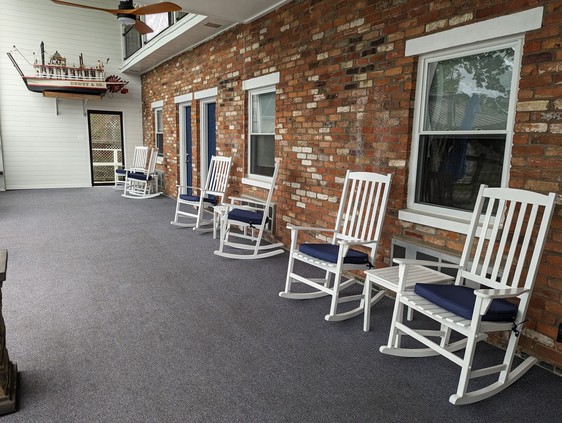 A row of white rocking chairs are sitting on a porch in front of Riverboat Inn.