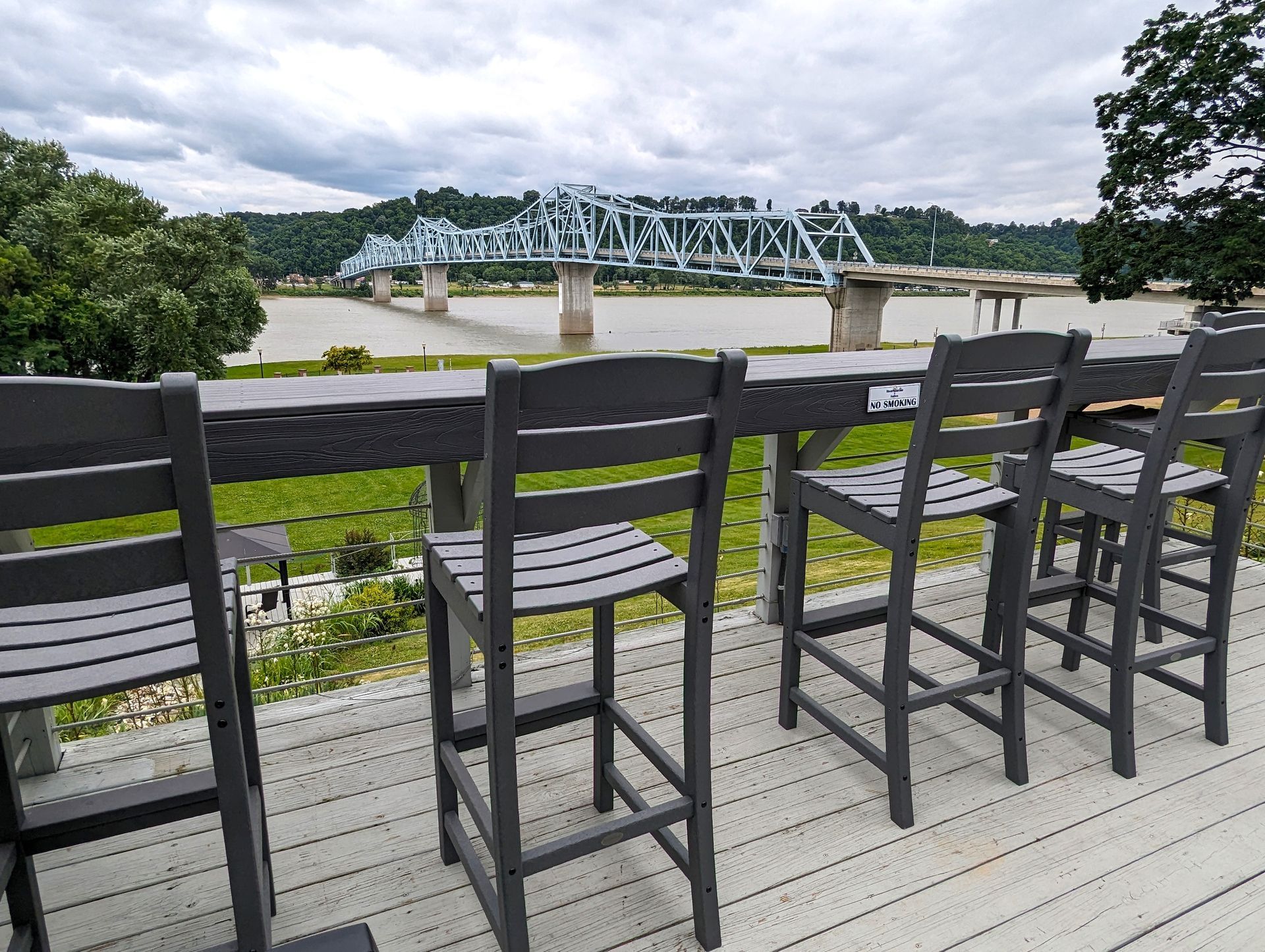 A row of chairs and a table on a deck with a bridge in the background.