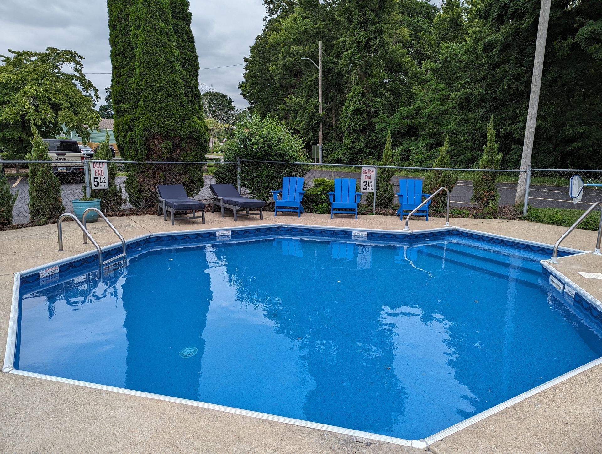 A large blue swimming pool surrounded by chairs and trees.
