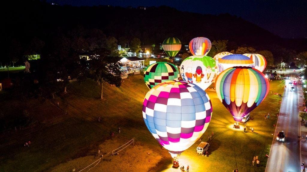 A group of hot air balloons are flying over a field at night.