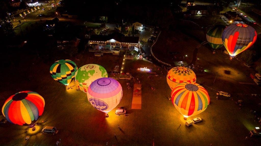A group of hot air balloons are flying over a field at night.