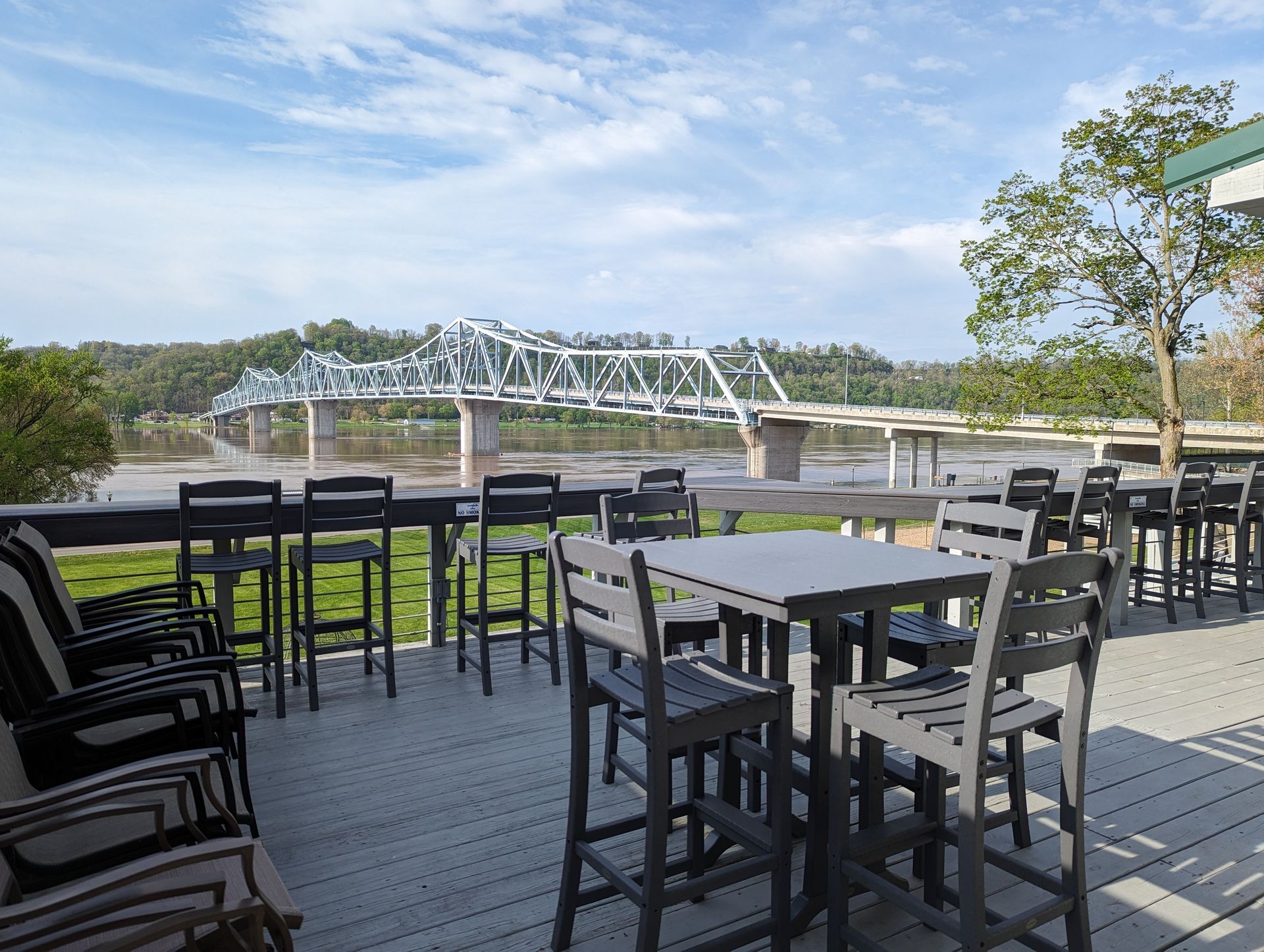 A deck with tables and chairs overlooking a river and a bridge.
