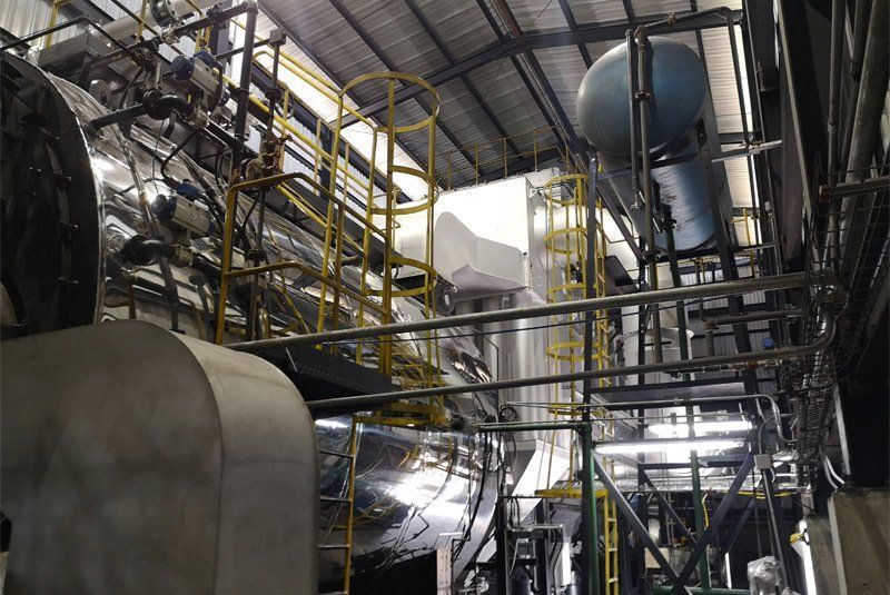 Interior industrial con grandes equipos metálicos, tuberías y una escalera de seguridad amarilla, probablemente una planta de fabricación.
